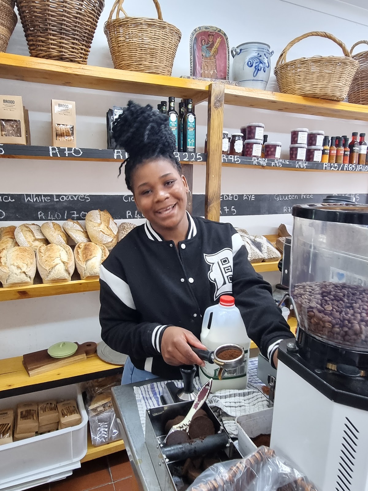 Smiling barista at BROOD preparing espresso with fresh sourdough loaves on display